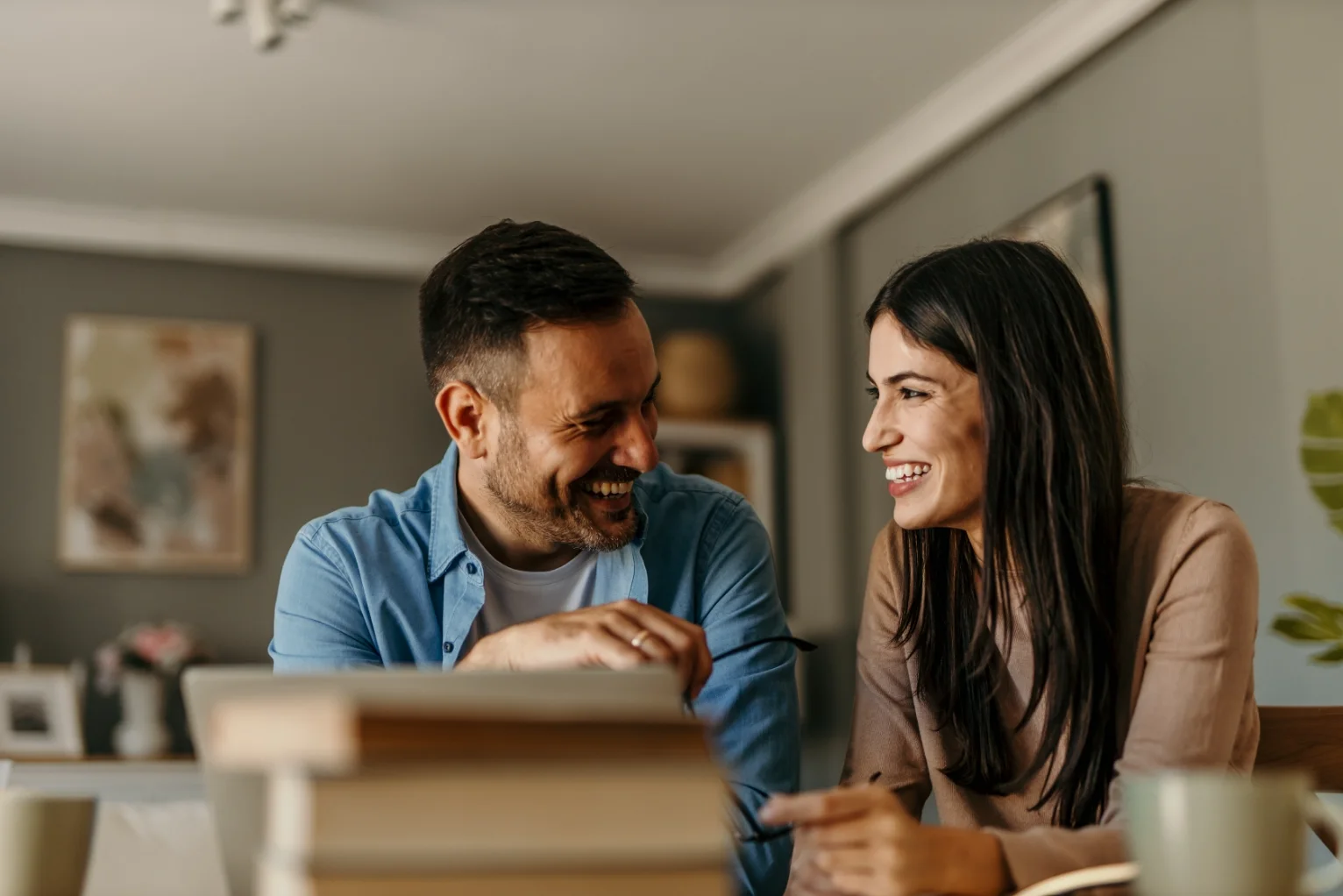 Young couple smiling while discussing financial documents in a living room setting.